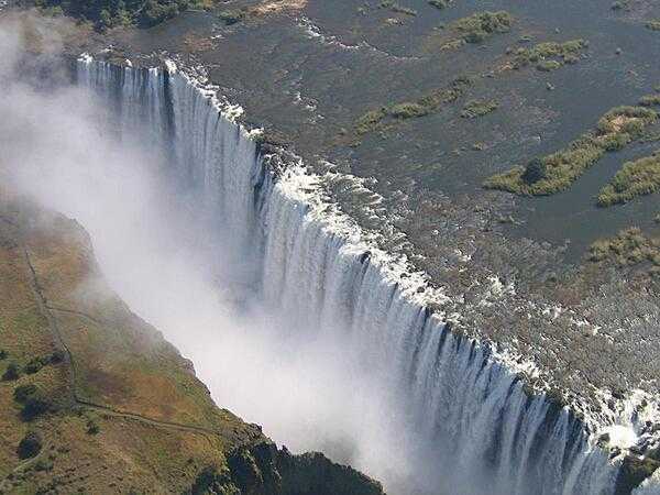 View of Victoria Falls on the Zambezi River as seen from the Zambian side. The falls are located on the border of Zambia and Zimbabwe. During flood season (February to April), the falls form the greatest sheet of falling water on earth. Victoria Falls is 1.7 km (1.1 mi) wide and 108 m (360 ft) high and is known locally as Mosi-oa-Tunya (The Smoke that Thunders).